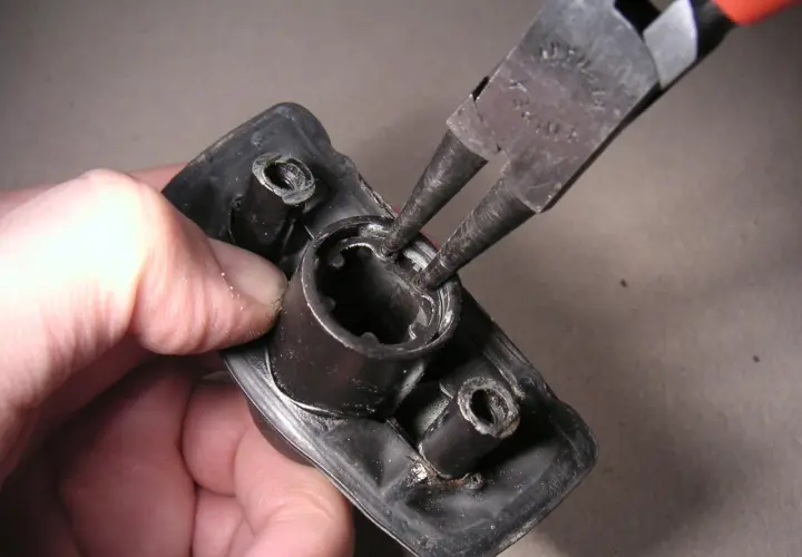 Mit einer Seegeringzange wird ein Sicherungsring aus einem schwarzen Bauteil entfernt.