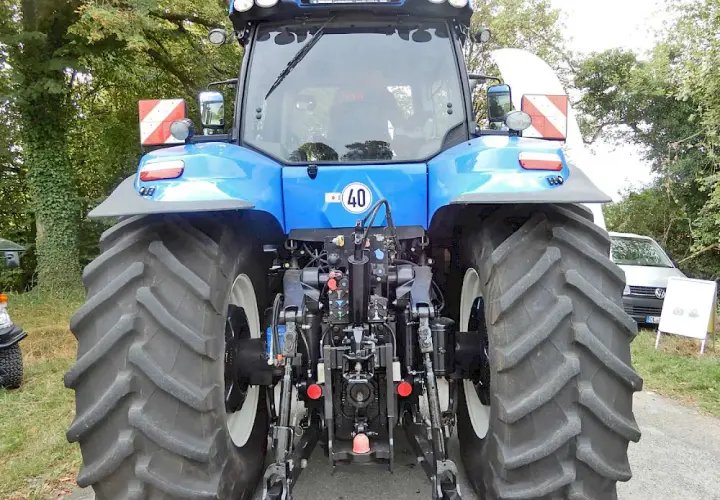 Blauer Traktor mit großen Reifen. An der Seite sind rot-weiße Warnschilder mit Beleuchtung angebracht.