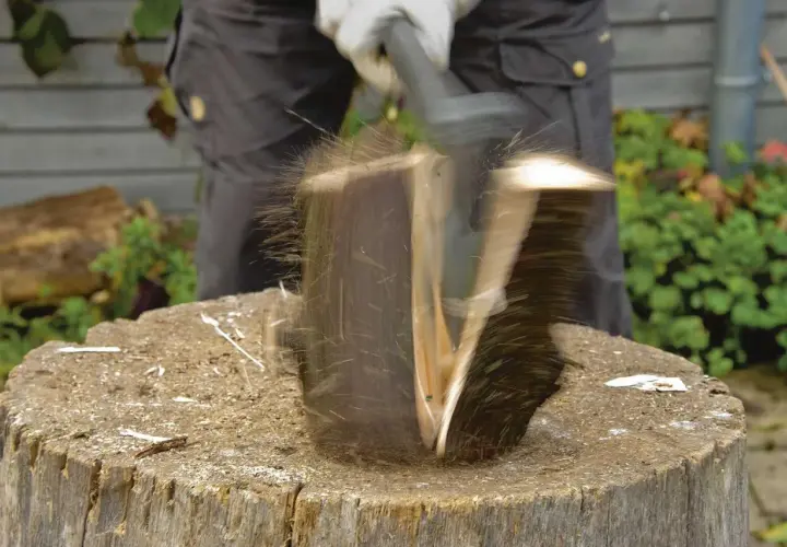 Ein Mann spaltet mit einem Keil einen Baumstamm. Holzsplitter fliegen durch die Luft.