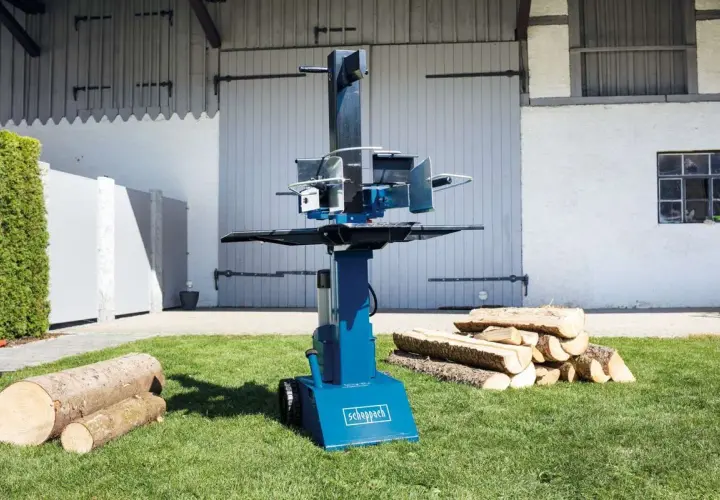 Scheppach Holzspalter Öl nachfüllen: Ein blauer Holzspalter steht auf einem Rasen, daneben liegen Holzscheite.