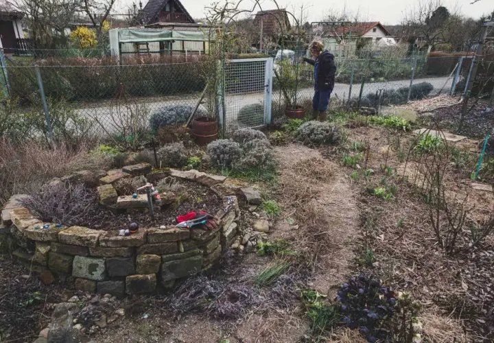Gartenarbeit im Frühling: Eine Frau steht neben einem Hochbeet, das mit Steinen gemauert ist. Was ist ein Mulcher? Er hilft, den Boden zu bedecken.