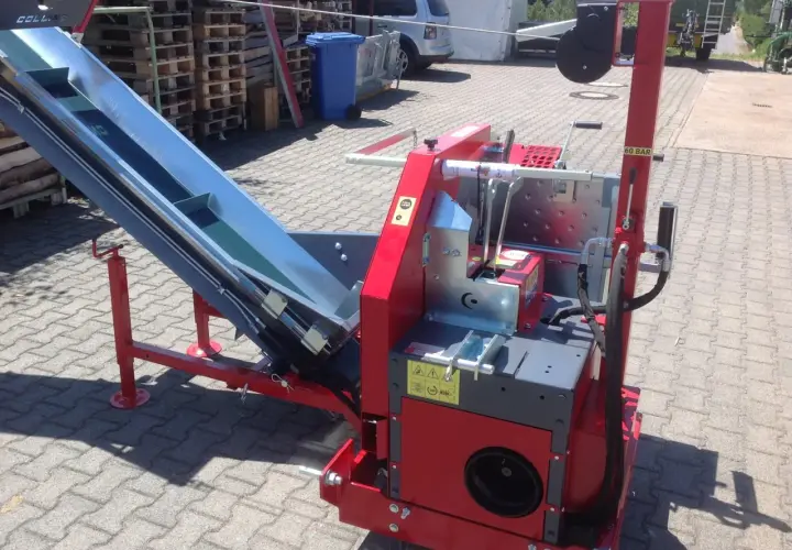 Rote Maschine mit einem langen, schrägen Förderband, bereit für den Einsatz. Diese Kreissäge mit Förderband ist ein robustes Gerät für die Holzverarbeitung.