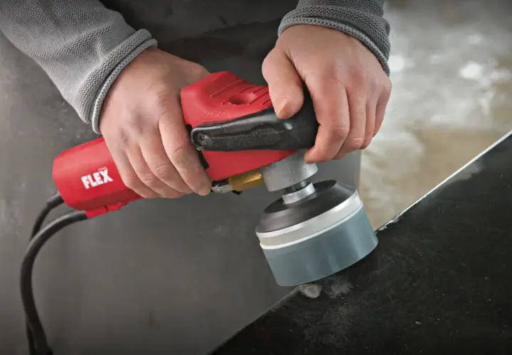 Präzises Stein schleifen mit einem roten Winkelschleifer von Flex. Staub wirbelt auf, während die Kante bearbeitet wird.