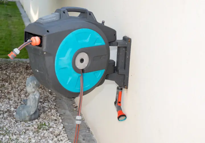 Ein schwarzer wandschlauchaufroller mit türkisfarbenen Akzenten hängt an einer weißen Wand. Ein Gartenschlauch ist teilweise aufgerollt.