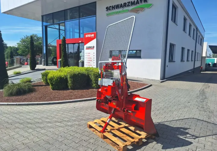 Roter Forstkran auf einer Palette vor einem Landtechnik-Gebäude. Ein robustes Gerät für den Einsatz im Wald, bereit für den Transport.