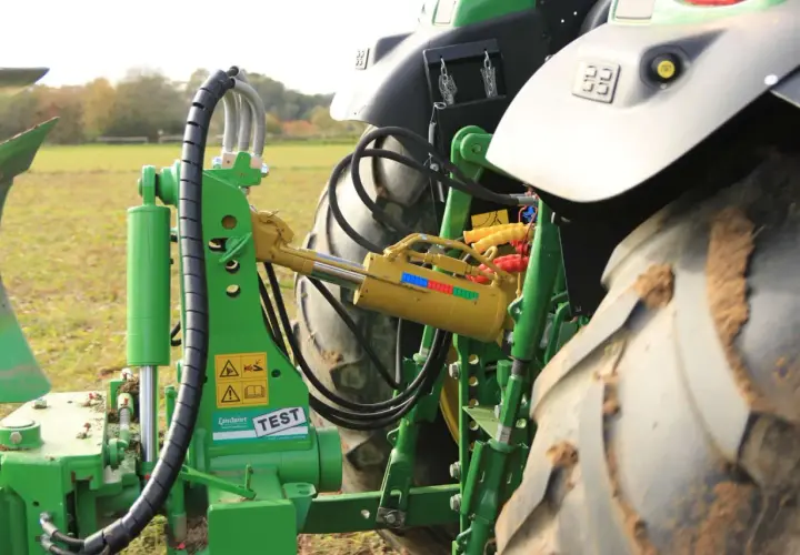Grüner Traktor mit angehängtem Pflug. Ein gelber Walterscheid Oberlenker mit Hydraulikzylinder ist sichtbar.