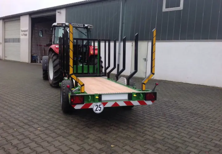 Ein roter Traktor mit einem neuen meterholzwagen mit kran steht vor einer Halle.