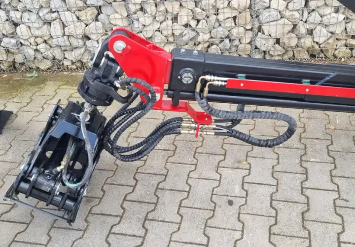 Detailaufnahme eines roten und schwarzen Schwenkwerks für Forstkran mit Greifer und Hydraulikschläuchen.