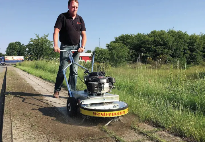 Mann mit Westermann Wildkrautbürste auf einem Gehweg, um Unkraut zu entfernen.