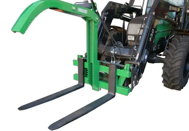 Grüner Greifer für Palettengabel, montiert an einem Traktor. Ideal zum sicheren Transport von Rundholz oder anderen sperrigen Lasten.