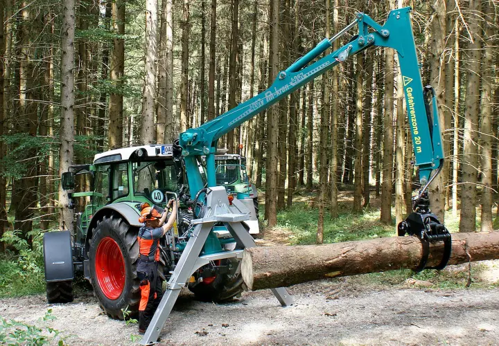 Ein Mann bedient den Kran eines Traktors im Wald. Das Schwenkwerk des Krans greift einen Baumstamm.