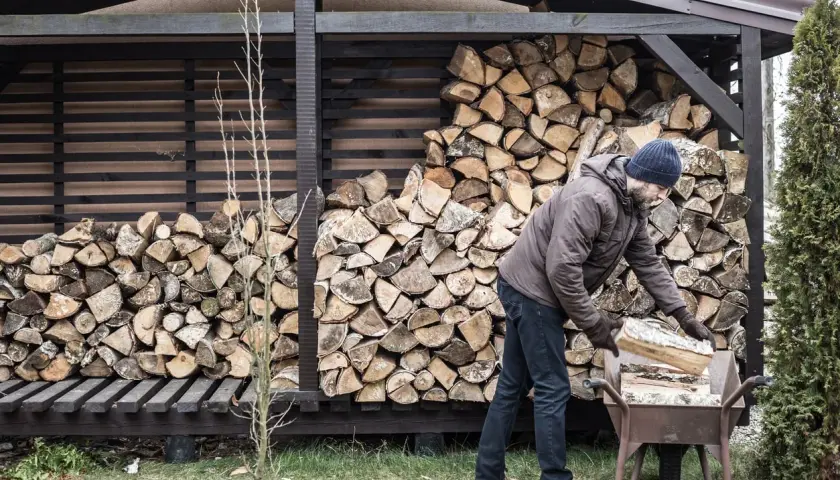 Mann mit blauer Mütze lagert anmachholz in einer Schubkarre. Der Holzstapel hinter ihm ist beeindruckend.