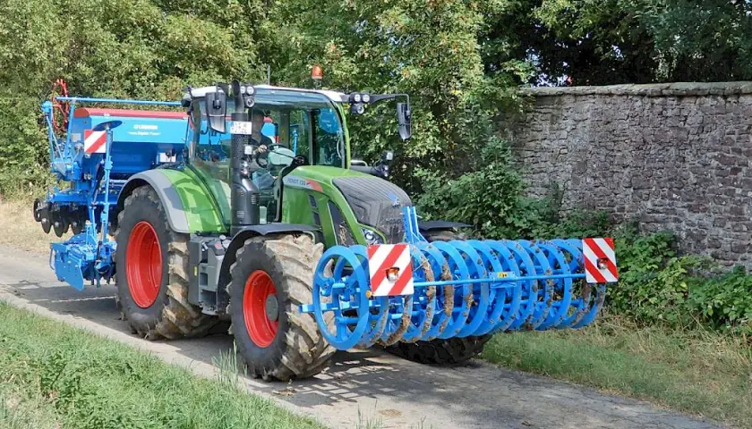 Grüner Traktor mit Anbaugerät und Warnstreifen, erinnert an eine mobile Parkwarntafel, fährt auf Feldweg.