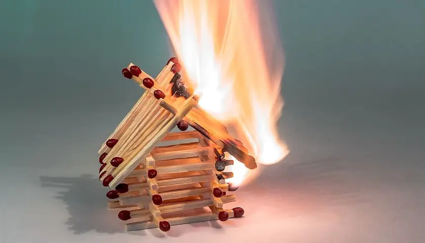 Ein Haus aus Streichhölzern brennt lichterloh. Die Flammen zeigen, ab wann Holz brennt.