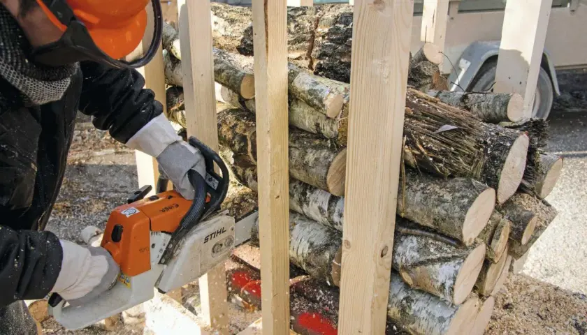 Mann mit Kettensäge bereitet brennholz sägen vor. Holzscheite sind gestapelt und werden für den Winter vorbereitet.