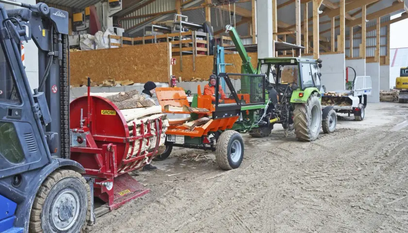 Holzspalter und Traktor mit Anhänger, bereit für den Transport. Die mobilen Förderbänder sind im Einsatz, um das Holz zu bewegen.