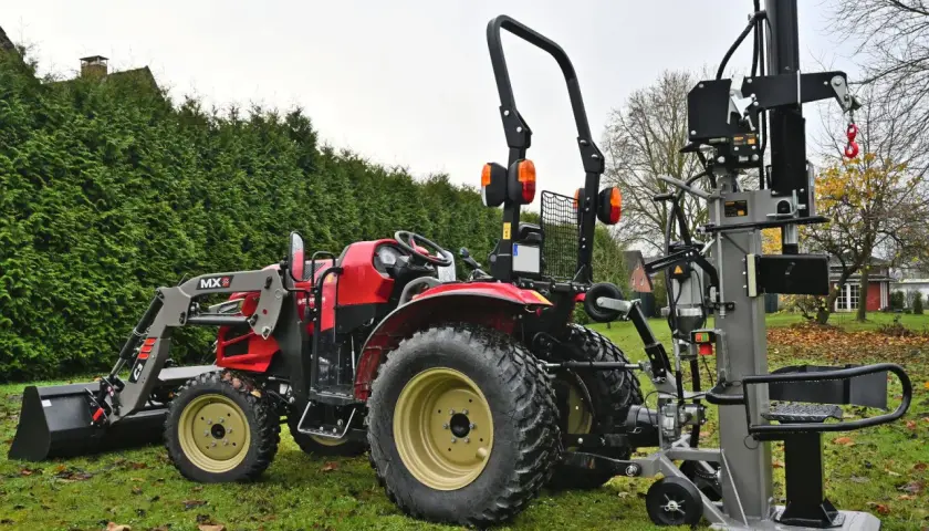 Roter Traktor mit Frontlader und einem liegenden Holzspalter gebraucht 30t im Garten.