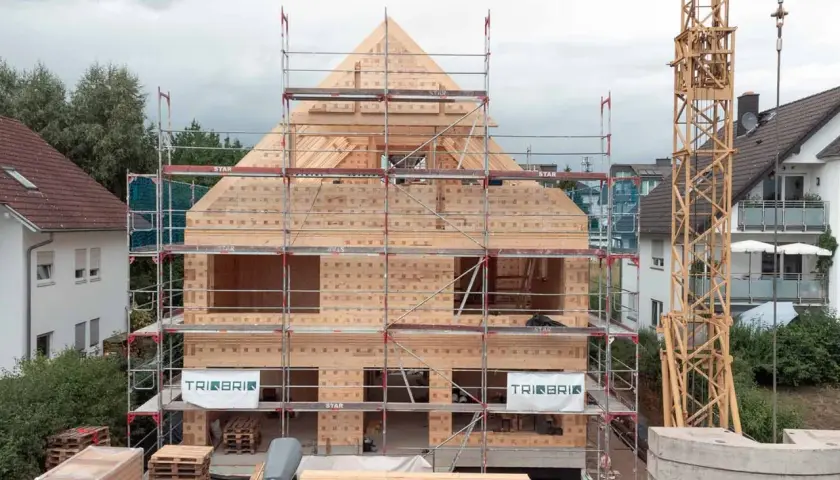 Holzbau im Wohngebiet: Ein Haus aus Holz wird mit Gerüsten und Kran errichtet.