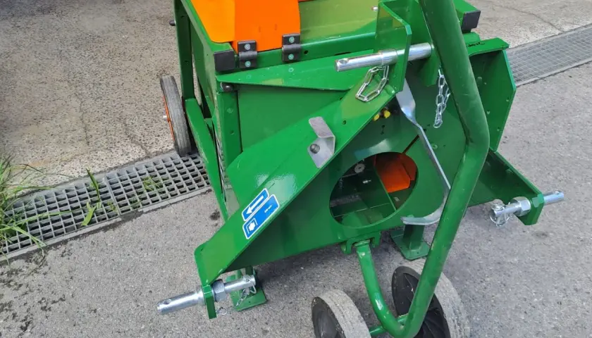 Grüne Wippsäge mit orangefarbenem Gehäuse, bereit für den Einsatz. Die Zapfwelle ist angeschlossen, um Holz zu zerkleinern.