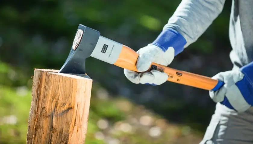Person mit Handschuhen hält Axt über Holzscheit, bereit, um zu zeigen, wie spaltet man holz.