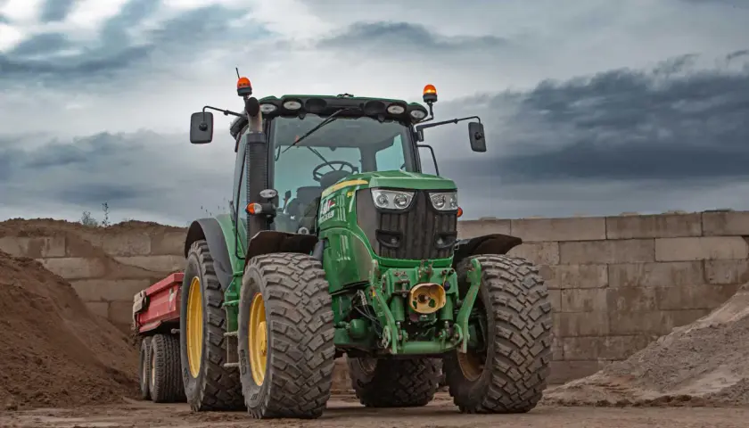 Grüner Traktor mit Anhänger, zwei orangefarbene Rundumkennleuchten auf dem Dach, bereit für den Einsatz auf der Baustelle.