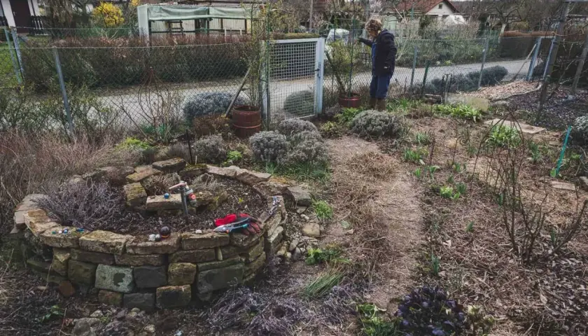 Gartenarbeit im Frühling: Eine Frau steht neben einem Hochbeet, das mit Steinen gemauert ist. Was ist ein Mulcher? Er hilft, den Boden zu bedecken.