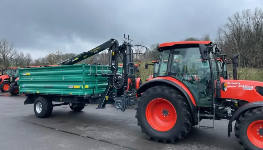 Ein roter Traktor mit einem grünen Anhänger und Ladekran steht bereit für den Einsatz.