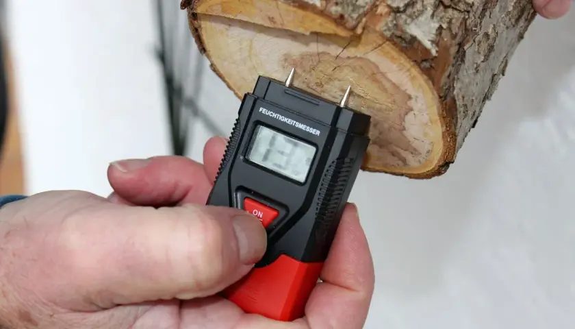 Ein Feuchtigkeitsmesser misst den Feuchtigkeitsgehalt von Brennholz. Die Anzeige zeigt 13%.