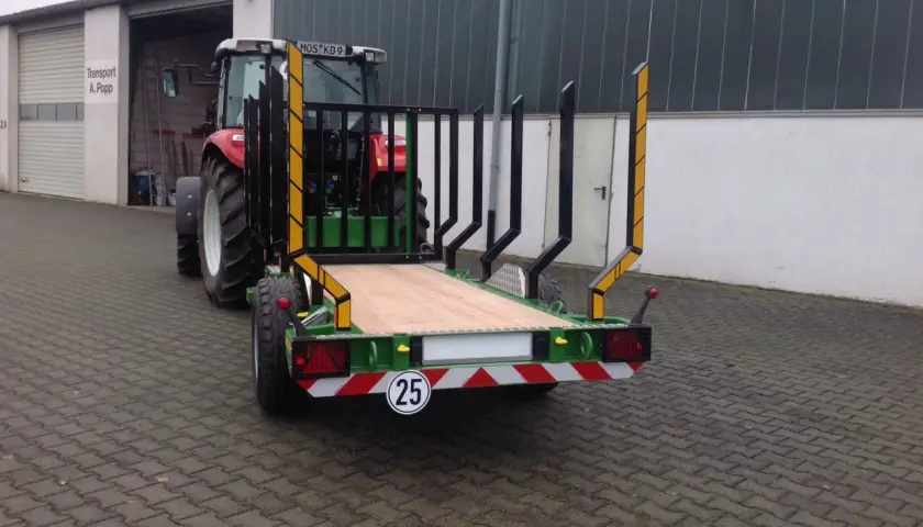 Ein roter Traktor mit einem neuen meterholzwagen mit kran steht vor einer Halle.
