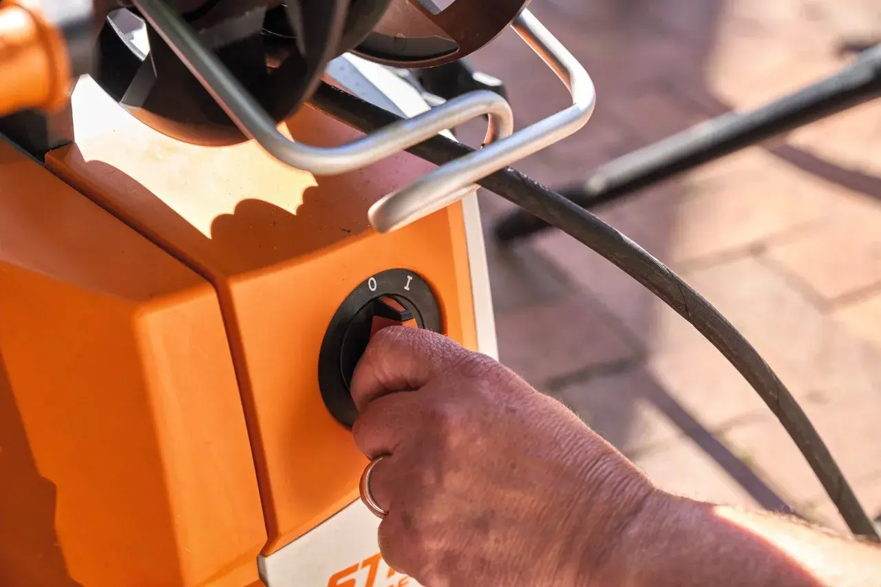 Hand dreht Schalter am orangefarbenen Hochdruckreiniger, bereit, ihn an den Wasserhahn anzuschließen.