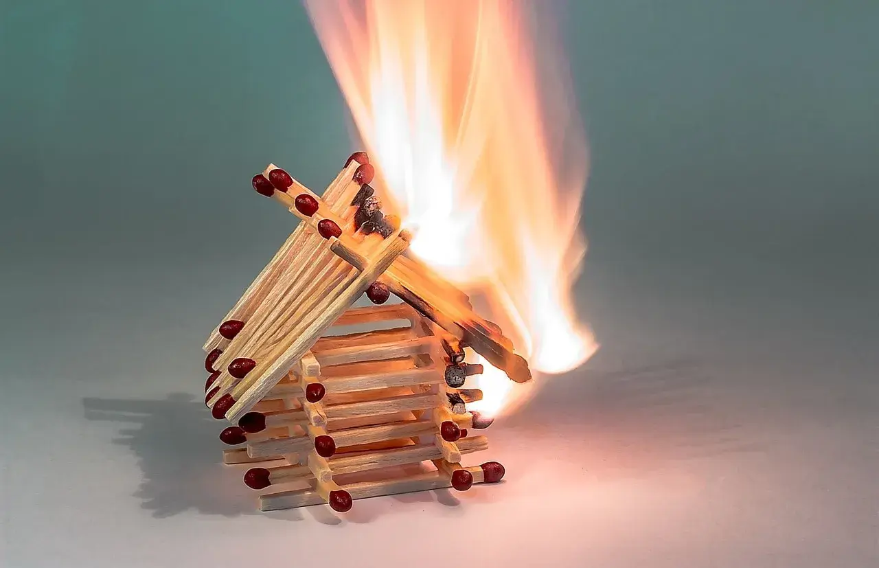 Ein Haus aus Streichhölzern brennt lichterloh. Die Flammen zeigen, ab wann Holz brennt.