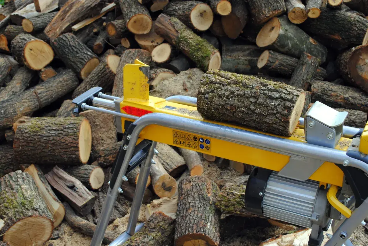 Ein gelber Holzspalter 1m liegt bereit, um den Stapel geschnittener Baumstämme zu bearbeiten.