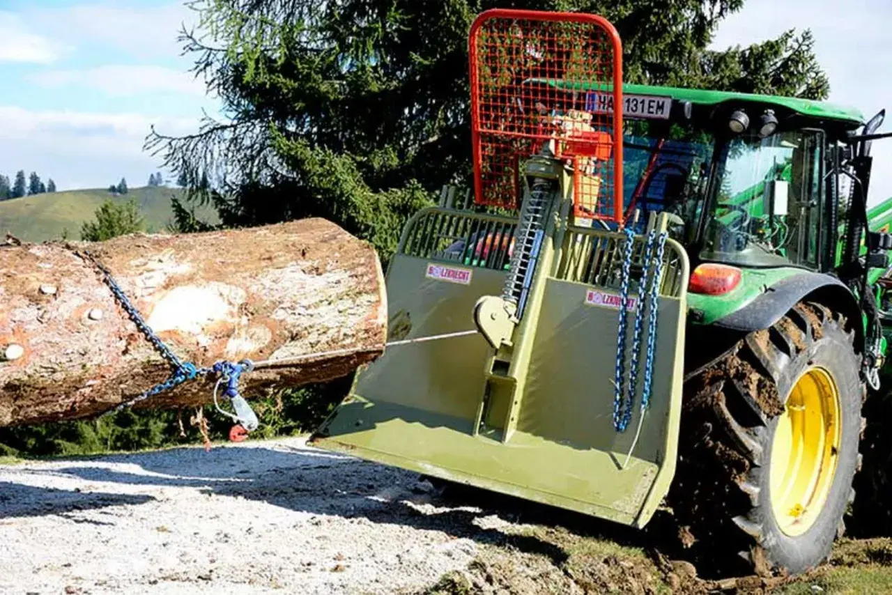 Ein Traktor mit einer **seilwinde** zieht einen Baumstamm aus dem **Wald**.