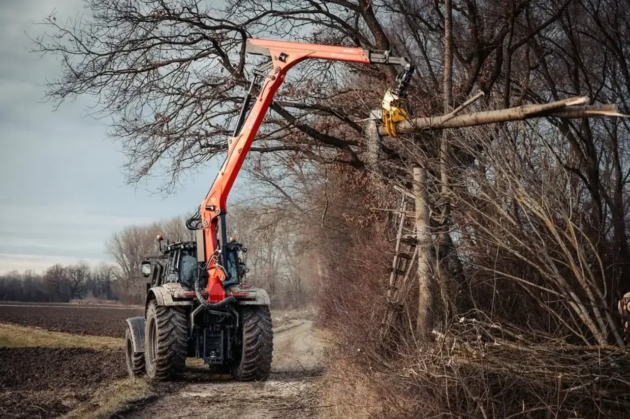 Ein Ladekran-Traktor mit orangefarbenem Ausleger schneidet einen Baumstamm in einem Wald.