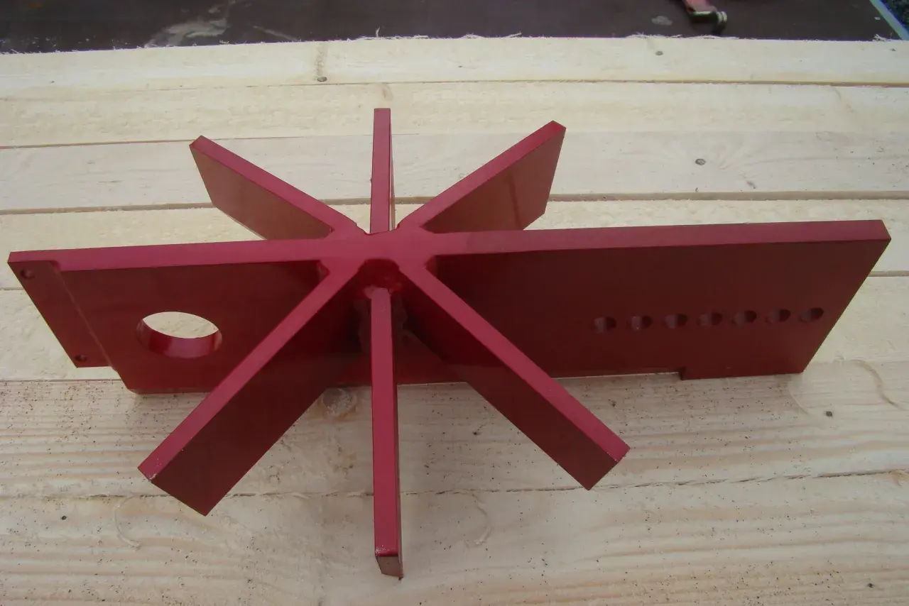 Rotes, sternförmiges Werkzeug mit acht Zacken, das wie ein spaltkreuz universal aussieht, liegt auf Holzbrettern.