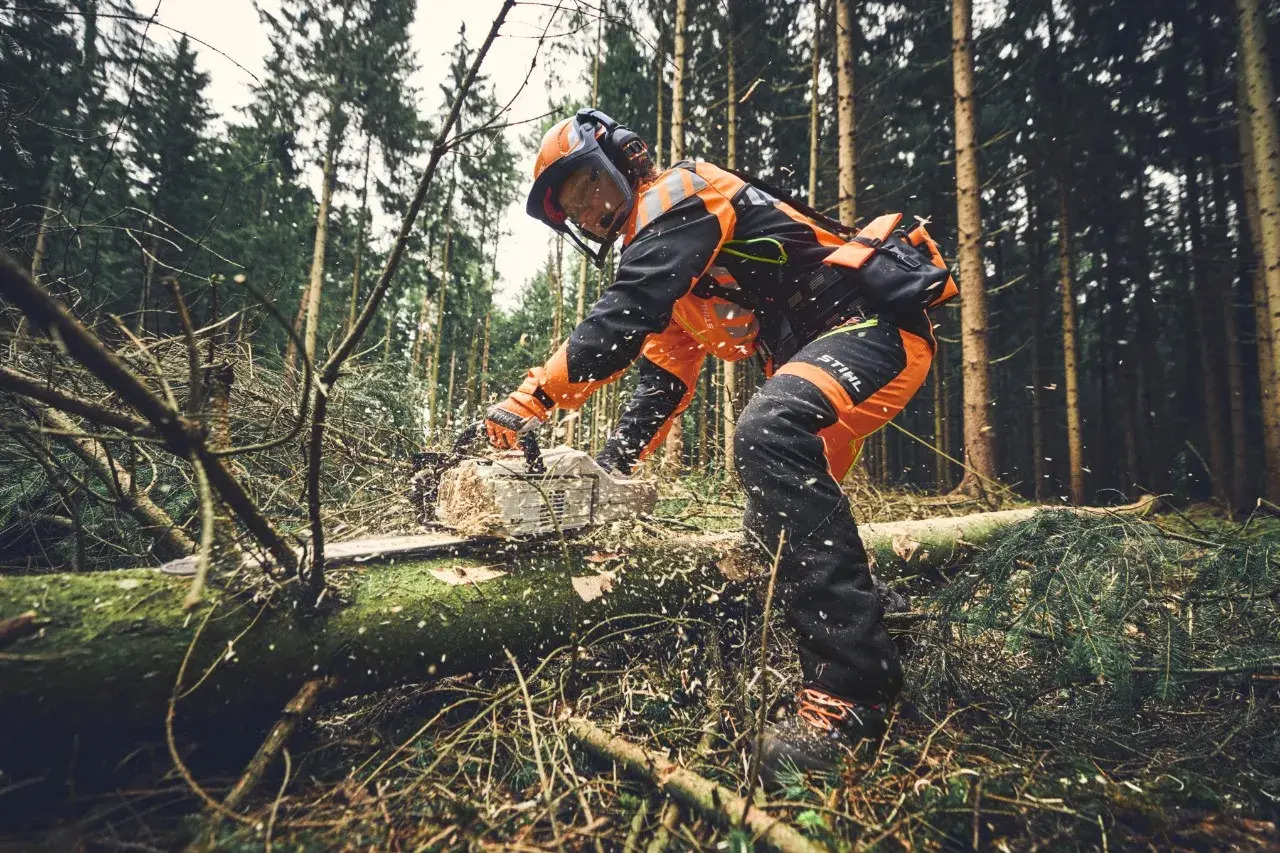 Forstarbeiter in Schutzkleidung arbeitet mit einer Kettensäge im Wald. PSA Forst schützt bei der Arbeit.