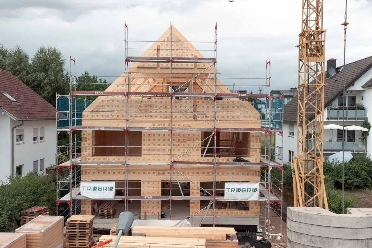 Holzbau im Wohngebiet: Ein Haus aus Holz wird mit Gerüsten und Kran errichtet.