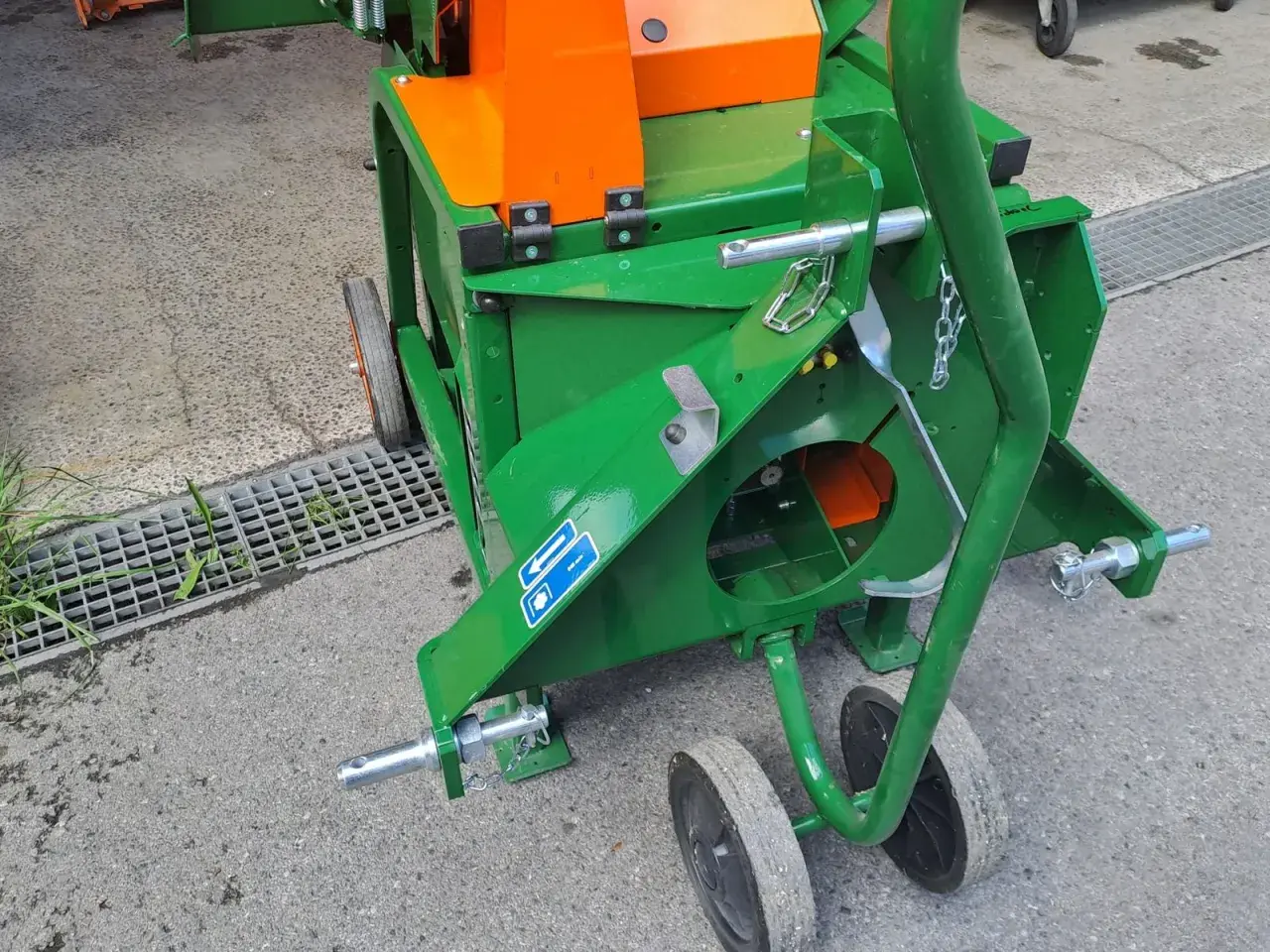 Grüne Wippsäge mit orangefarbenem Gehäuse, bereit für den Einsatz. Die Zapfwelle ist angeschlossen, um Holz zu zerkleinern.