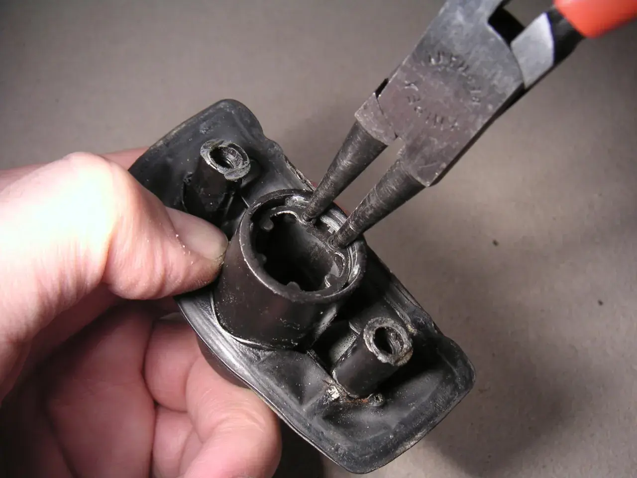 Mit einer Seegeringzange wird ein Sicherungsring aus einem schwarzen Bauteil entfernt.