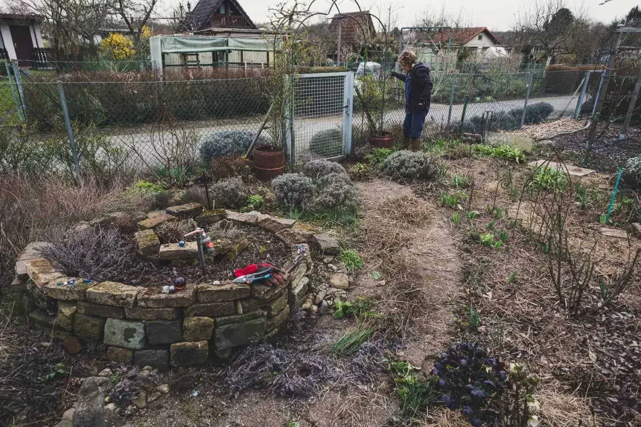 Gartenarbeit im Frühling: Eine Frau steht neben einem Hochbeet, das mit Steinen gemauert ist. Was ist ein Mulcher? Er hilft, den Boden zu bedecken.