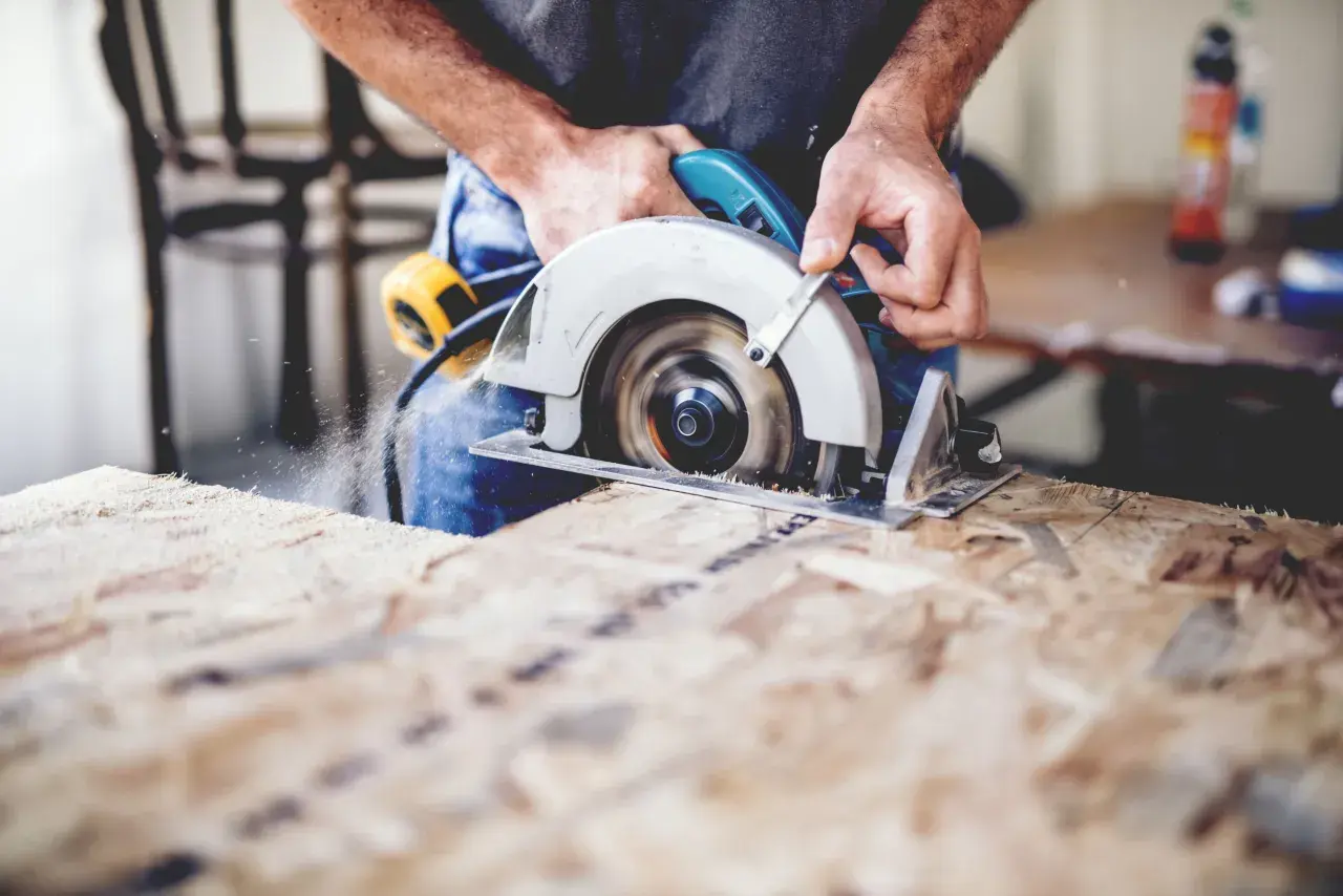 Ein Handwerker sägt mit einer **Baukreissäge** Holz. Sägespäne fliegen durch die Luft.
