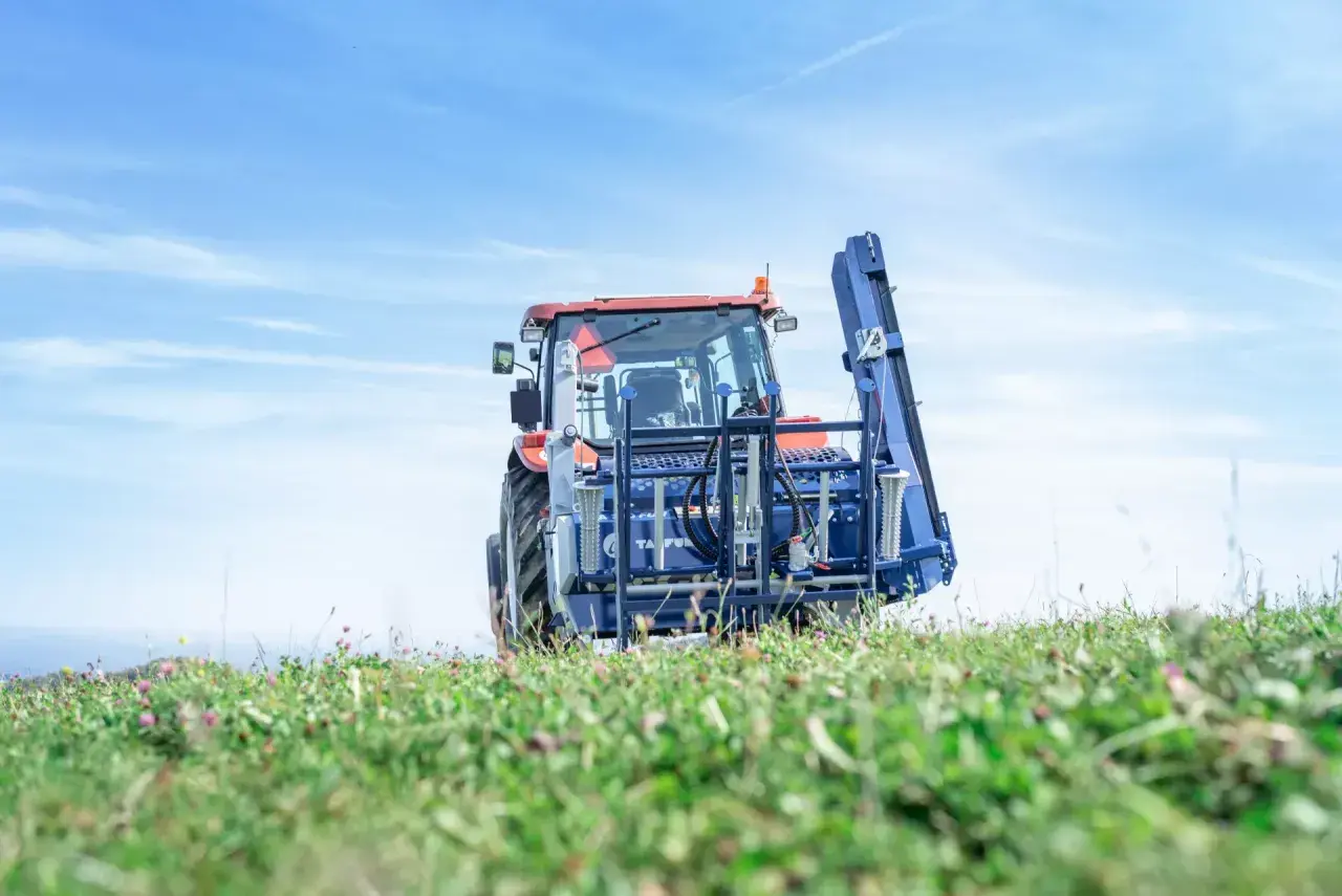 Traktor mit Tajfun RCA 480 auf einem grünen Feld unter blauem Himmel.