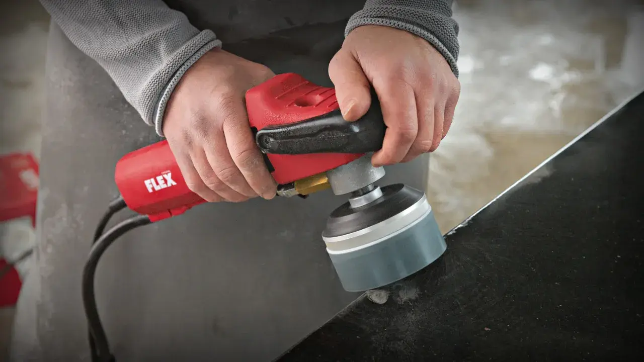 Präzises Stein schleifen mit einem roten Winkelschleifer von Flex. Staub wirbelt auf, während die Kante bearbeitet wird.
