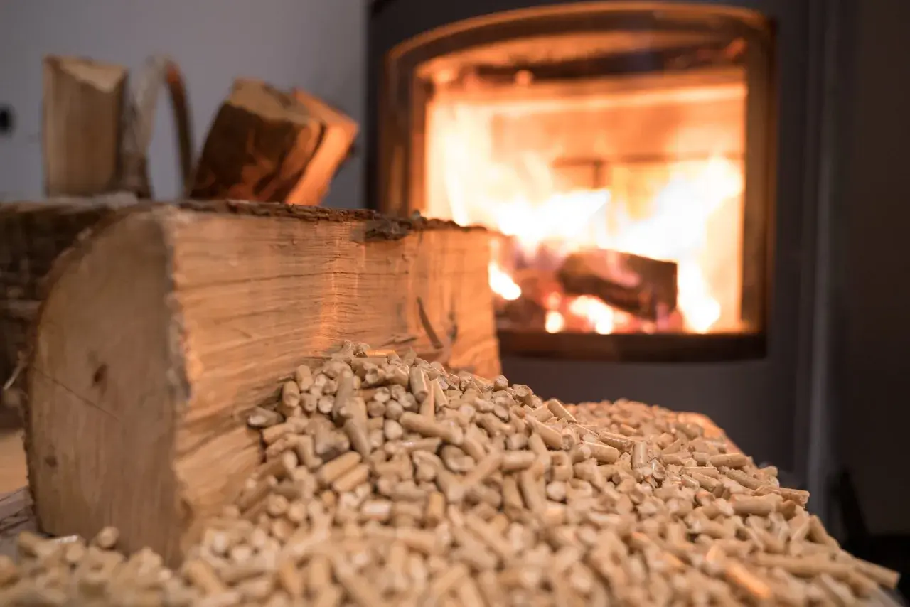 Holzscheite und Pellets liegen bereit, während im Kamin das Feuer lodert. Bauholz im Kamin verbrennen sorgt für wohlige Wärme.