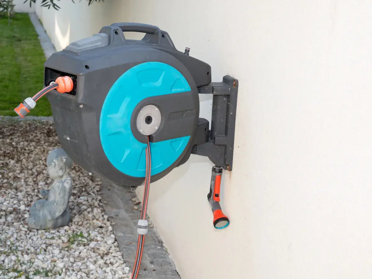 Ein schwarzer wandschlauchaufroller mit türkisfarbenen Akzenten hängt an einer weißen Wand. Ein Gartenschlauch ist teilweise aufgerollt.