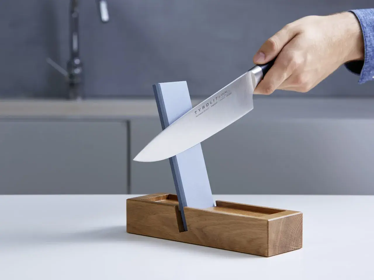 Ein Messer wird auf einem Schleifstein geschärft, der in einem Holzständer steckt. Dieser Schleifstein ist ein wichtiger Helfer, um die Schneide scharf zu halten, fast wie ein **dichtungsschaber** für die Klinge.