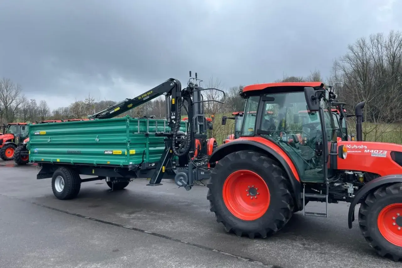Ein roter Traktor mit einem grünen Anhänger und Ladekran steht bereit für den Einsatz.