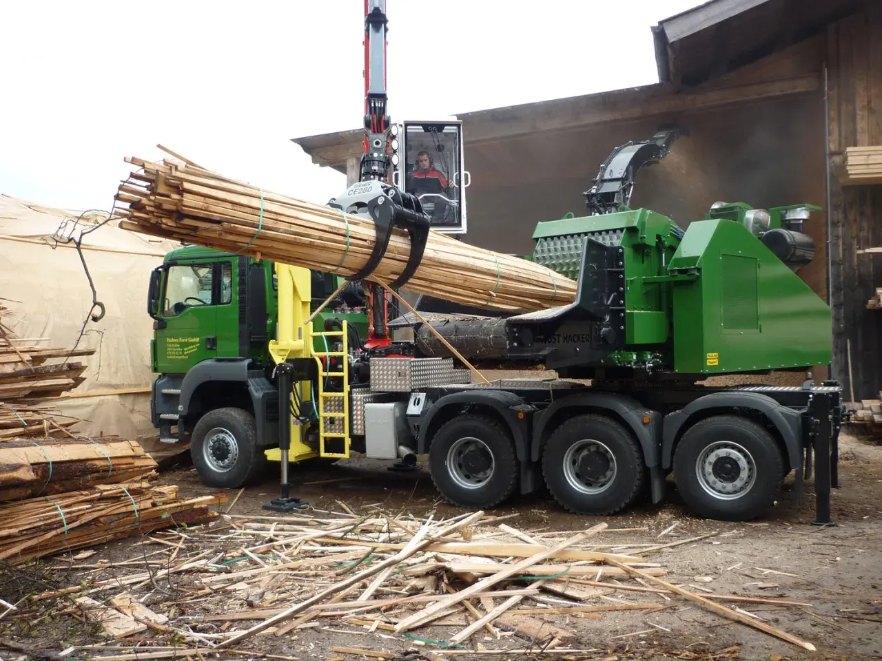 Grüner Holzhacker LKW mit Kran lädt Holzstämme. Der Hacker zerkleinert Holz zu Hackschnitzeln.