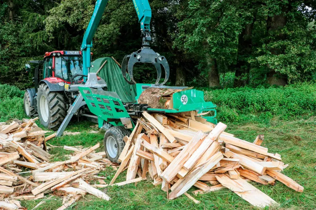 Ein Traktor mit einem Holzspalter, der gerade einen Baumstamm zerteilt. Ein gebrauchter Schichtholzspalter im Einsatz.