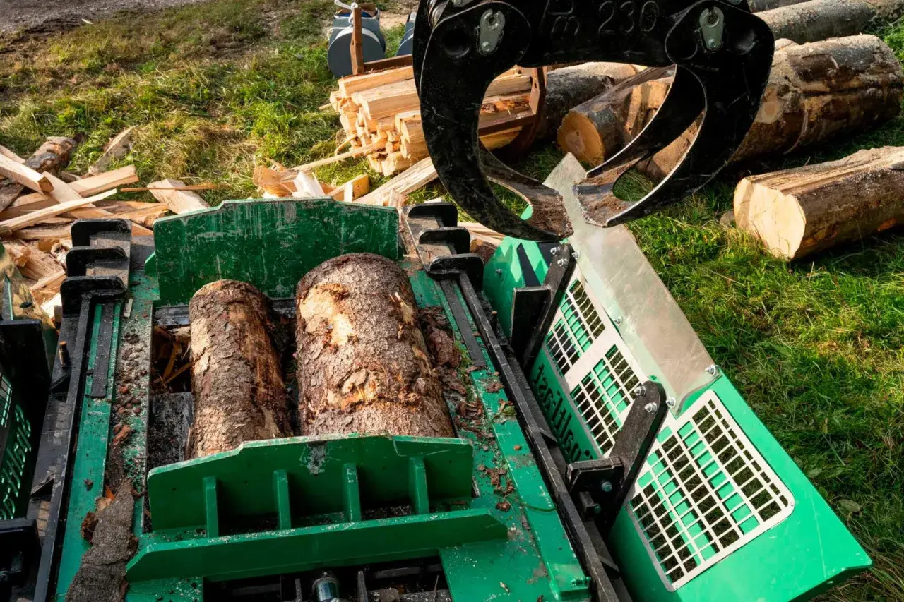 Ein Schichtholzspalter bereitet zwei Baumstämme für die Verarbeitung vor. Ein Greifer hält weitere Holzscheite bereit.